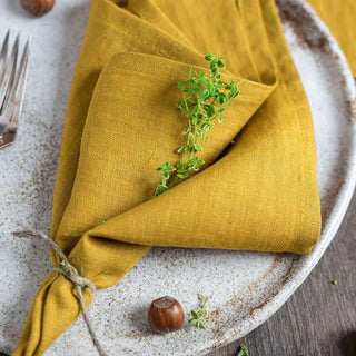 Mustard yellow linen table napkin layered over a rustic ceramic plate.