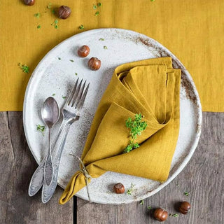 Mustard yellow linen table napkins styled with a rustic ceramic plate for a bright, natural dining space.