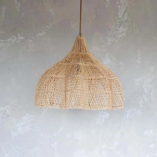 Natural handwoven rattan pendant light with dome-shaped silhouette and airy open weave, suspended against a textured grey wall.