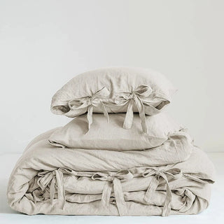 Natural beige linen bedding set with a duvet cover and two pillowcases tied with ribbon bows.  Perfect for a modern, Boho, Nordic or coastal bedroom styling.