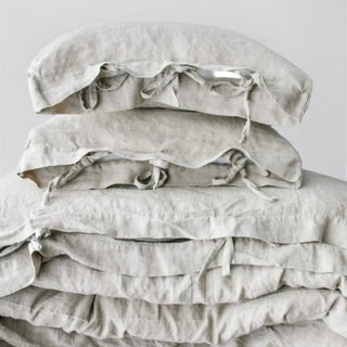 Natural linen bedding set with tie closures, styled on a bed with two pillows and a cozy duvet, creating a calm, minimalist bedroom look.