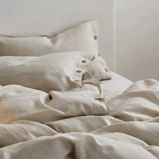 Beige linen pillows and duvet cover with coconut buttons, styled in a modern, minimalist bedroom.