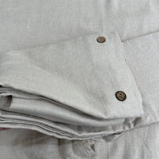 Close-up of a folded beige linen pillowcase with coconut buttons and a matching duvet cover.