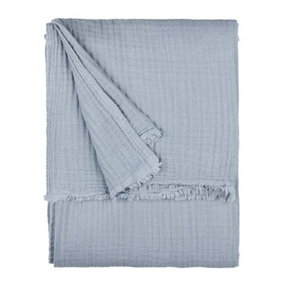 A folded light blue muslin blanket with fringed edges for layering on beds and sofas.
