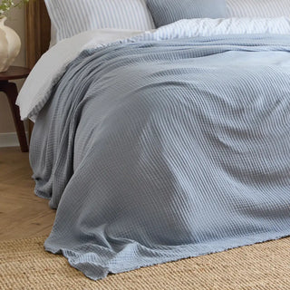 Blue textured muslin blanket draped on a bed  in a calm bedroom setting.