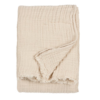 Beige cotton muslin blanket with frayed edges for draping on beds or sofas.