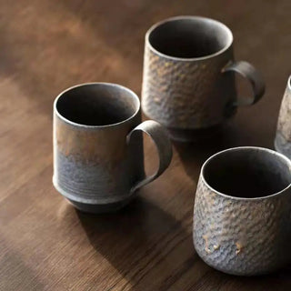 Handmade stoneware mug with a bronze metallic glaze, inspired by wabi-sabi aesthetics, displayed on table top.