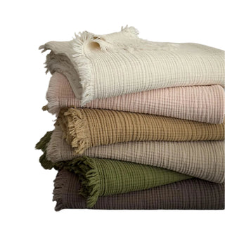 Lightweight cotton muslin throws in soft pastel colours, folded neatly with visible gauze layers.