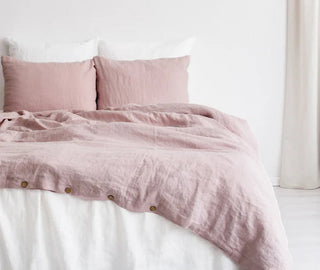 Pink linen duvet cover with button closure and matching pillowcases styled on a minimalist bed.