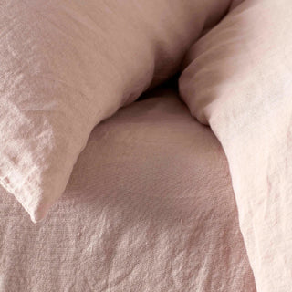 Close up of pink linen duvet cover, sheet and matching pillowcases styled on a bed.