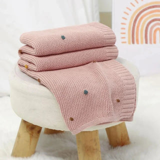 bBibi Cotton Knit Baby Blanket in soft pastel pink, folded neatly on a rustic wooden stool.