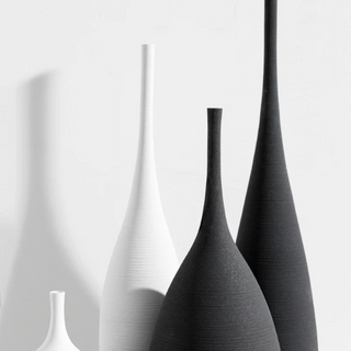 A set of Ren Handmade Ceramic Vases in black and white, featuring sleek, elongated necks and organic, curved bases. These minimalist, sculptural vases are perfect for modern, Japandi, and wabi-sabi home décor, adding an elegant contrast with their monochrome design. Ideal for dried flowers or as standalone art pieces, crafted with fine ceramic texture for a luxurious, handmade finish. Styled against a sunlit wall with soft shadows, enhancing their artistic appeal.