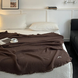 Chocolate brown fringed cotton throw draped over a bed.