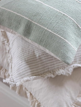 Sage green cotton cushion with white stripes for layering on sofas and beds in calm, natural interiors.