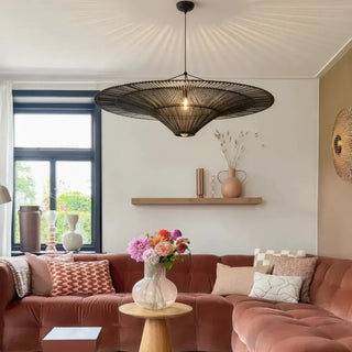 Black handwoven rattan pendant light with a sculptural funnel silhouette and warm ambient lighting in a contemporary living room.