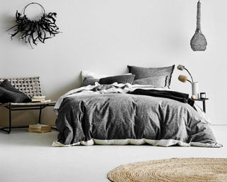 Scandi bedroom interior featuring charcoal linen bedding and pillows, natural round jute rug, wire mesh pendant light and minimalist chair.