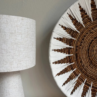 A close-up of a woven decorative wall plate with a circular brown base and white geometric starburst accents.