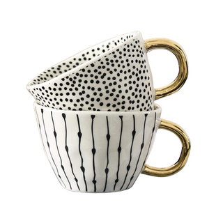 Handmade white ceramic cups with black dotted motif and a gold handle, minimalist and artistic in style.
