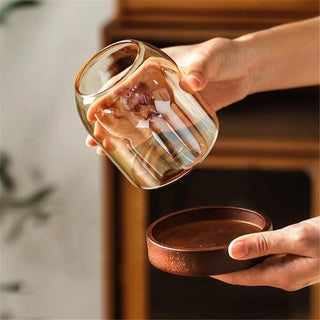 Minimal amber glass utensil holder with wooden base for chopsticks and cutlery.