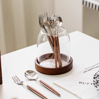 Clear glass utensil holder with wooden base on kitchen countertop