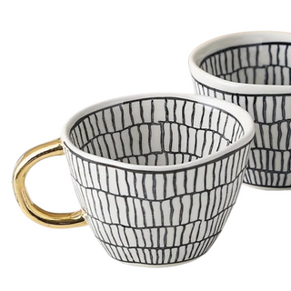 Handmade ceramic cup with black and white geometric design and a gold handle, minimalist and artistic in style.