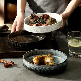 Three embossed ceramic deep plates in blue, white, and black from the Suki collection by Arkaim Home.