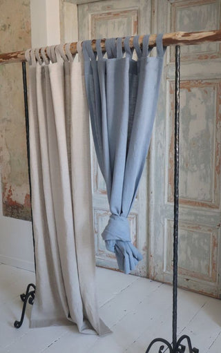 Tab-top, natural Oma linen curtain hanging in rustic interior space.