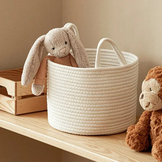 Small white cotton rope storage basket with handles for storing toys and styled in a nursery.