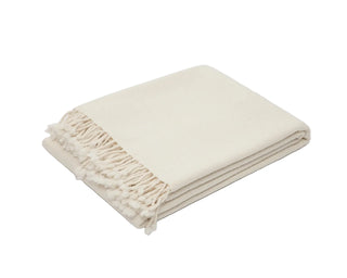 A folded cream-colored woven throw blanket with fringed edges.