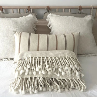 Fine merino wool blanket in soft natural white displayed on a neutral linen bed, premium wool throw.