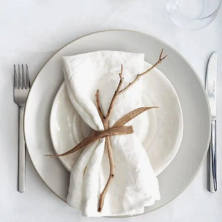 White linen table napkin styled with white ceramic plates on a minimal dining table.