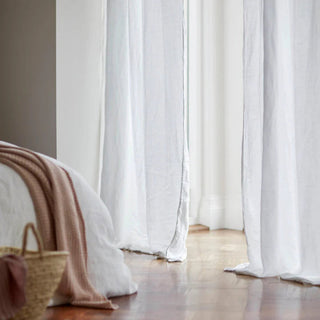 White linen curtain softly draped to the floor in a sunlit minimalist bedroom.