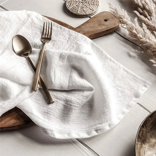 White linen table napkin draped over a wooden board and styled with cutlery.