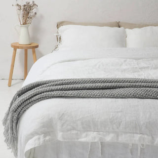 White linen bedding set with tie closures, styled on a bed with two pillows and a cozy duvet, creating a calm, minimalist bedroom look.