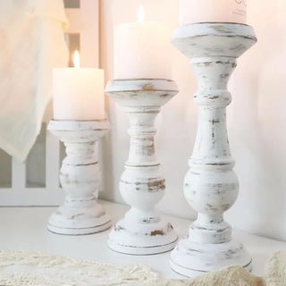 Three distressed white wooden candle holders with white pillar candles, arranged on a console.