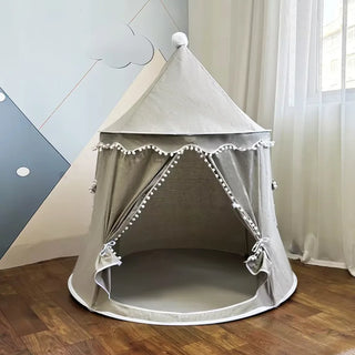 Large grey kids teepee play tent with pom pom trim set up by a window