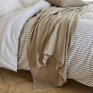 Nori latte cotton muslin throw draped over the end of a bed