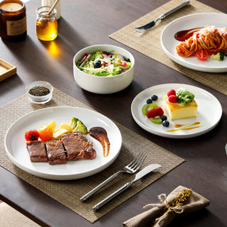 White ceramic dinnerware set laid for dinner with steak, salad and dessert on a wooden table