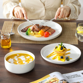 White ceramic dinnerware set with a bowl of soup, pasta and a glass of water on a dark table