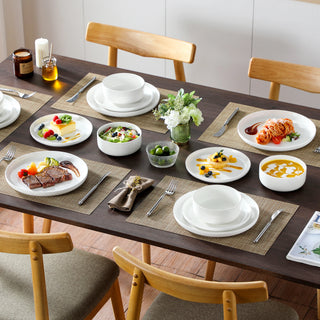 White ceramic dinnerware set laid for four on a wooden dining table